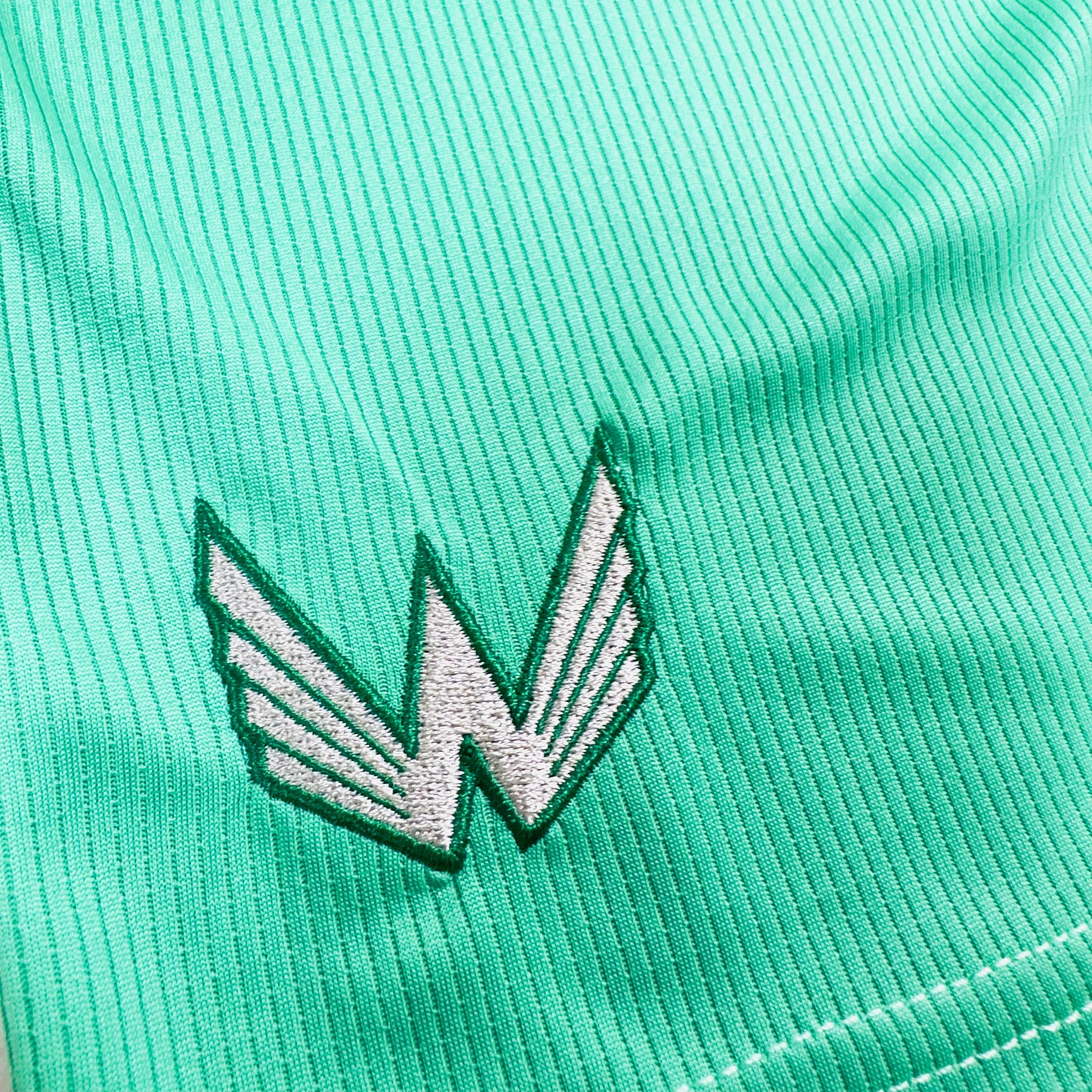 Close-up of a green sports jersey with an embroidered logo on a textured fabric background.